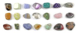 21 different types of healing stones - in three neat rows randomly placed on a white background including citrine, blue lace agate, amazonite, jasper, amethyst, ametrine, emerald, rose quartz